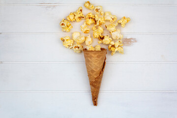 Top view of ice cream cone with popcorns on white wooden table