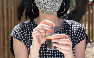 Woman with social face mask holding a expresso coffee