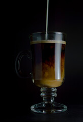 cafe con leche cayendo sobre fondo obscuro en taza de vidrio estilo irlandes