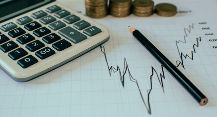 stack of coins, calculator and pencil on a graph chart background 