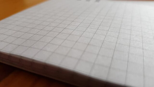 New open notebook. Checked paper. In the distance lies a pen. Macro side view
