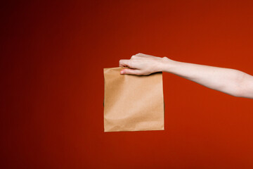 Female hand holds a brown paper bag on a red background. Advertising banner concept for delivery and gift service.