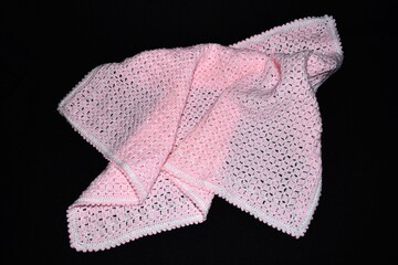 Handmade crocheted pink and white baby blanket on black background.