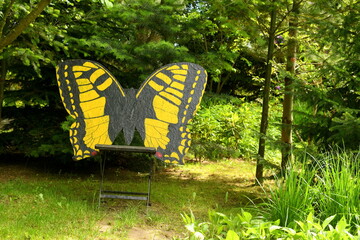 A close up on a handmade silhouette of a black and yellow butterfly leaning against a small chair seen in the middle of a decorative well maintained garden on the Polish countryside in summer