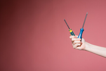 Female hand on a pink background holds two screwdrivers. Advertising banner for construction stores.
