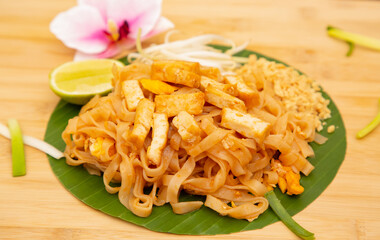 Pad Thai is Thai food Noodle and tofu mixed with tamarind sauce and bean sprouts and spring onion in white dish put on the banana leaf in wooden background