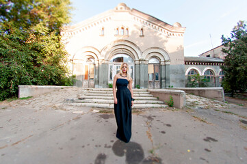 Beautiful woman model with long blond hair in a black evening dress with open neckline decoration...