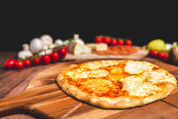 Homemade freshly baked Pizza Margherita with melted mozzarella on the top on a wooden board with lots of decorative vegetables. Concept of fresh hot pizza with free space for your text/decorations.