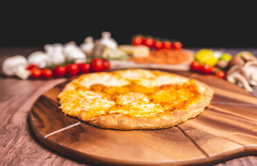 Homemade freshly baked Pizza Margherita with melted mozzarella on the top on a wooden board with lots of decorative vegetables. Concept of fresh hot pizza with free space for your text/decorations.