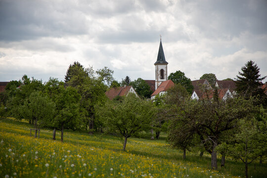 Kirchturm und Wiesenlandschaft unter bew&ouml;lktem Himmel