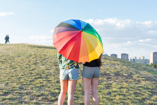 Two girls under an umbrella in lgtbi colors. Back view, copy space.