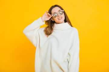 Cute lovely young woman in round sunglasses standing and sending kiss over yellow background