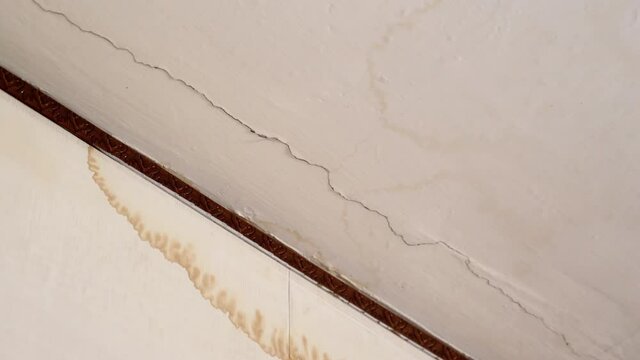 Water cracks on the plaster ceiling after heavy rain or leakage from the upper neighbor apartment. Large brown dirty spots on the plaster ceiling, water droplets destroying roof. Mold formation