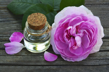 Obraz na płótnie Canvas Rose essential oil in a glass bottle with fresh pink rose flower on old wooden table.Spa, skin care or aromatherapy concept.Organic cosmetics.Selective focus. 