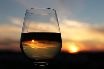Glass with white wine on beautiful sunset background, sun and sky are reflected in alcohol drink. Concept of celebration, evening party at resort, romantic dinner outdoors