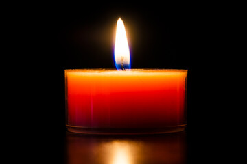 Orange burning candle in a glass tealight beautiful close-up isolated on black.