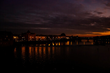 Naklejka premium A view from Charles Bridge where sun sets over the river of Vltava. Reflection of lights and sunset makes the picture perfect.