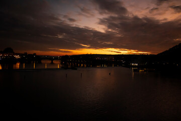 Fototapeta premium A view from Charles Bridge where sun sets over the river of Vltava. Reflection of lights and sunset makes the picture perfect.