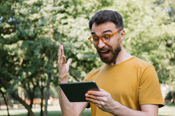 Fototapeta premium Emotional man using digital tablet, shopping online, watching movie. Excited guy looking at screen, celebration success, sport betting concept 