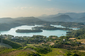 View of the reservoir lake and green field, from the top of the high hill. Background mountains and sunset