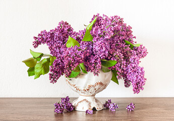 Bouquet of purple lilac in a antique vase on the table.