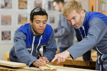 carpenter teaching apprentice how to measure wood