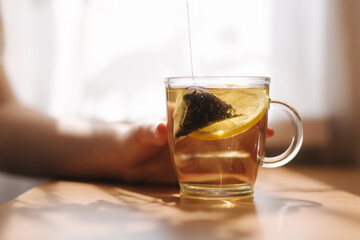 Hand of woman making black tea with lemon on wooden table