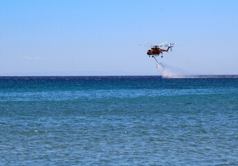Helikopter straży pożarnej pobiera wodę z morza  - obrazy, fototapety, plakaty