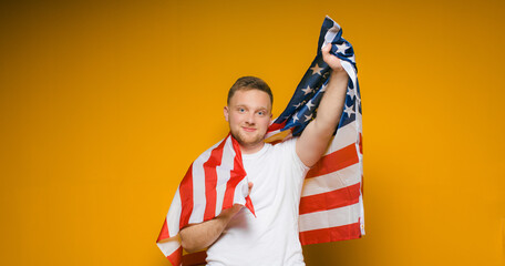 Fototapeta na wymiar Celebrating an Independence day. Stars and Stripes. Young man with the flag of the United States of America isolated on yellow studio background. Looks happy and proud as a patriot of his country