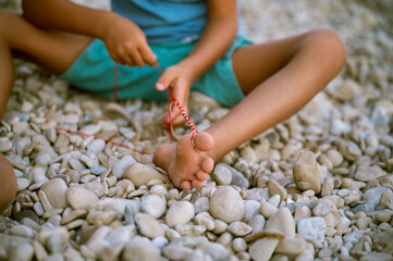 Toddler boy making a knotted bracelet on the beach