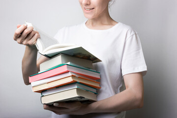 Girl in a white shirt holds a lot of books in the hands of a neutral background. Reading, page turning