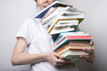 A girl in a white T-shirt holds a lot of books in her hands on a neutral background. Education,...