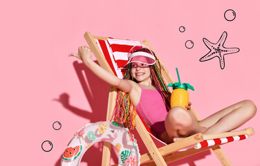 Fototapeta premium Smiling girl with colorful hair in swimsuit and sun cap relaxing on sunbed with pineapple and showing thumb sign with finger