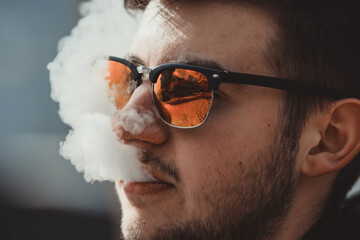 Vape teenager. Portrait of young handsome guy smoking an electronic cigarette outside. Bad habit that is harmful to health. Vaping activity. Close up.