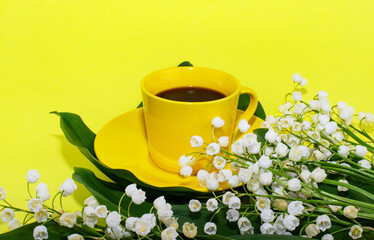 Yellow cup with coffee on a yellow background. Lily of the valley flowers