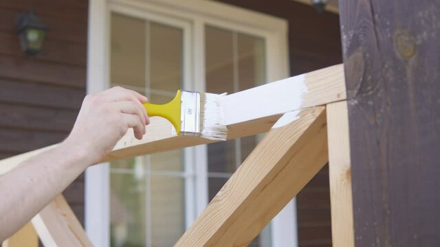 Close up of young man hand painting wooden fence with the brush