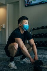 Naklejka premium Young asian male squatting in the gym wearing mask, during COVID19