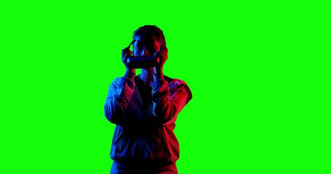 Excited young asian teen gamer wearing virtual reality glasses and holding controllers having fun enjoy playing vr game in Silhouette colourful UV lighting over green screen background.