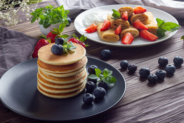 Pancakes with fresh blueberry, strawberry, mint and basil leaves on brown wooden background. Tasty breakfast.