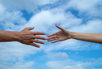 Giving a helping hand. Hands of man and woman on blue sky background. Lending a helping hand. Solidarity, compassion, and charity, rescue. Hands of man and woman reaching to each other, support