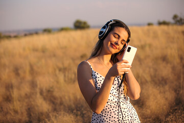 Sweet blonde girl listen happy music outdoors in summer sunset