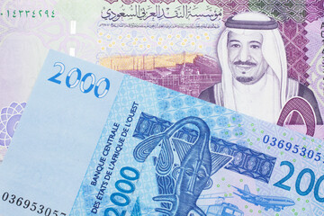 A close up image of a blue, West African franc bank note with a five Saudi riyal bank note in macro