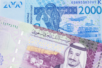 A close up image of a blue, West African franc bank note with a five Saudi riyal bank note in macro