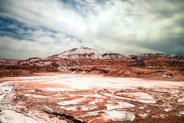 The pink and white riverbed in Atacama desert with red hill in the background and beautiful clouds above #1