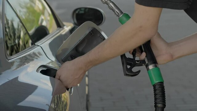 Close up of hand and fuel nozzle into automobile's tank. Fuel, gas station, petrol prices concept. Filling car with gas fuel at station pump.