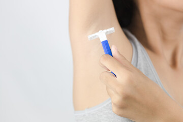 Asian young woman holds a razor on hand to shave her armpit hair
