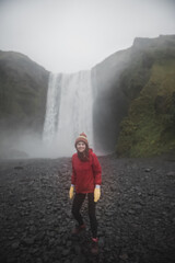 Iceland landscape photo of brave girl who proudly standing with his arms raised in front of water wall of mighty waterfall.