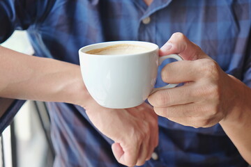 Close-up man hand holding coffee cup foam, hand holding cup of coffee while sitting in cafe 	