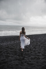 Fototapeta na wymiar bride in white clothes stands in a black cave on a black sand beach near the Atlantic Ocean in Iceland