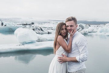 Wedding in Iceland. A guy and a girl in a white dress are hugging while standing on a blue ice floe on a background of mountains